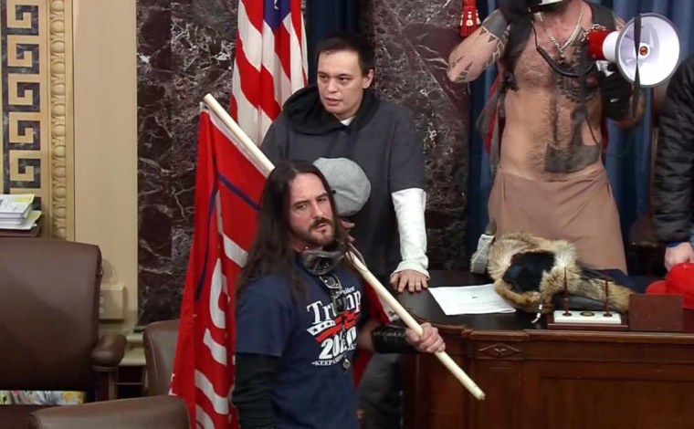 Image: Paul Allard Hodgkins carries a large red "Trump 2020" flag inside the Senate chamber during the Capitol riot on Jan. 6.