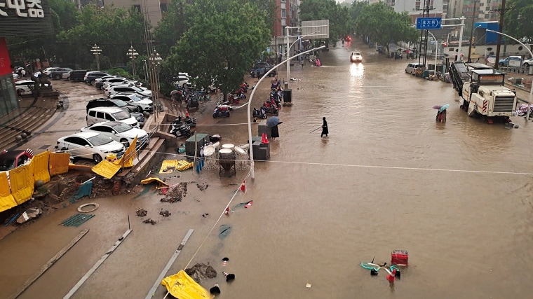 Image: People wade through floodwaters on a road amid heavy rainfall in Zhengzhou