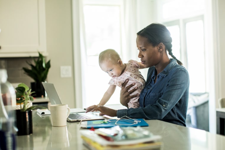 Mother holding baby while using laptop/working from home