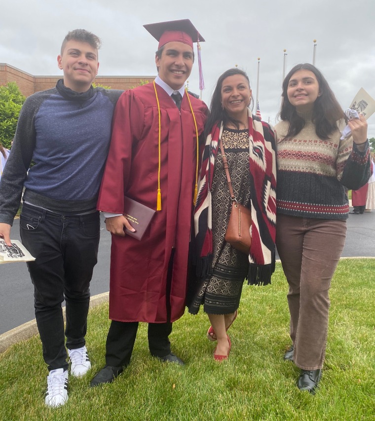A family poses on grass with a graduate in a red cap and gown