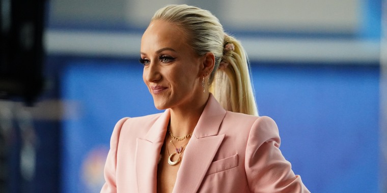 Nastia Liukin sits in a pink blazer in front of a blue background.