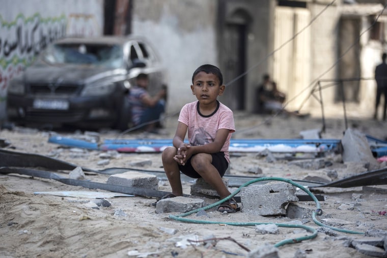 Image: A Palestinian boy sits looking at others inspecting the damage of their shops following Israeli airstrikes on Jabaliya refugee camp, northern Gaza Strip