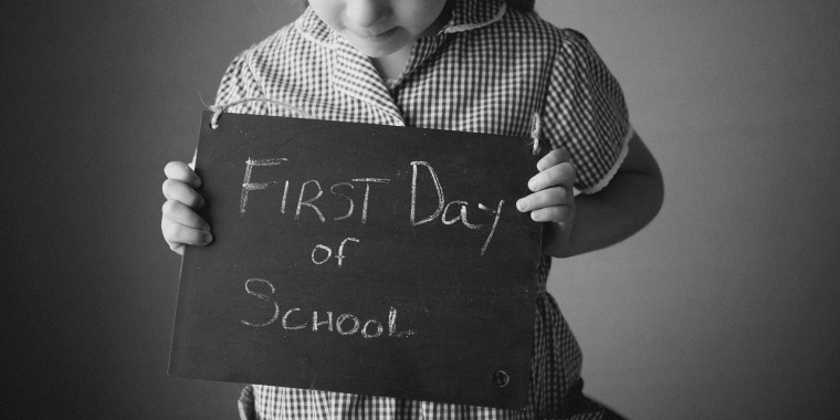 4-year-old girl with braids holds a handwritten chalkboard sign that says, "First Day of School."
