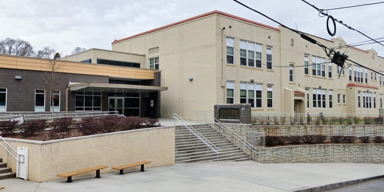 The front of a beige three story elementary school with steps outside