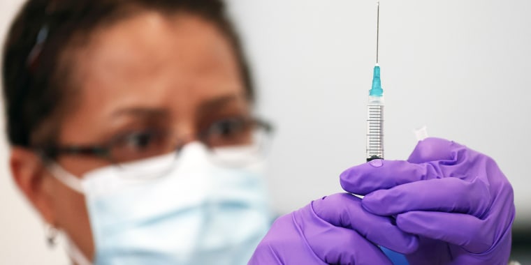Pharmacist with purple rubber gloves looks at a syringe filled with clear liquid
