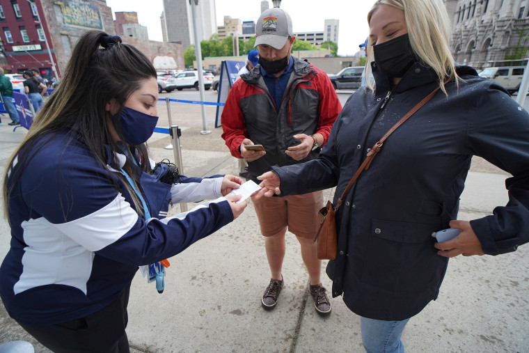 A woman in a face mask hunches over another woman's outstretched hand holding a vaccine card, reading