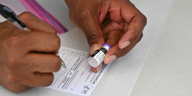 A woman fills out a vaccination card while holding a vial of the covid-19 vaccine