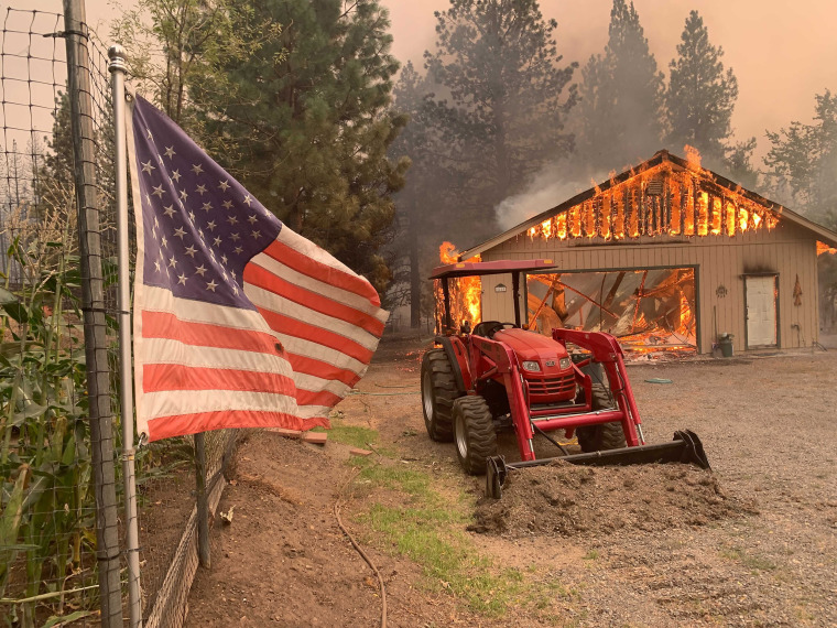 A red tractor is left behind as a home burns outside of Taylorsville in Plumas County, Calif., that was impacted by the Dixie Fire Friday, Aug. 13, 2021. The U.S. Forest Service said Friday it's operating in crisis mode, fully deploying firefighters and maxing out its support system as wildfires continue to break out across the U.S. West. The agency says it has more than twice the number of firefighters working on the ground than at this point a year ago, and is facing \"critical resources limitations.\" An estimated 6,170 firefighters alone are battling the Dixie Fire in Northern California, the largest of 100 large fires burning in 14 states, with dozens more burning in western Canada. It has destroyed more than 1,000 structures in the northern Sierra Nevada.