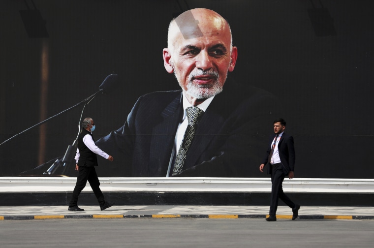 People walk near a mural of President Ashraf Ghani at Hamid Karzai International Airport in Kabul, Afghanistan, on Aug. 14, 2021.