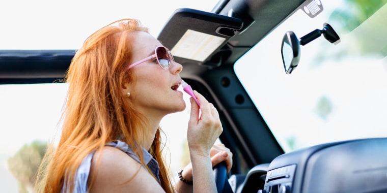 Woman doing make up in car, looking in her rearview mirror