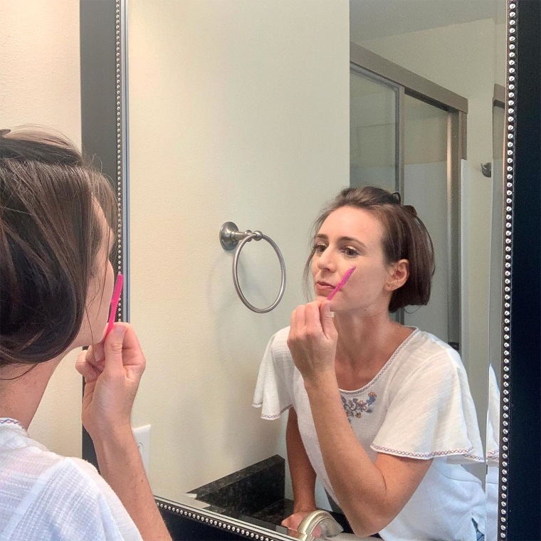 Writer Katie Jackson looking in the mirror, using a small blue face razor