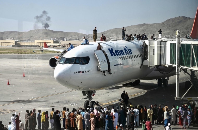 Image: Afghan people climb atop a plane as they wait at the Kabul airport in Kabul