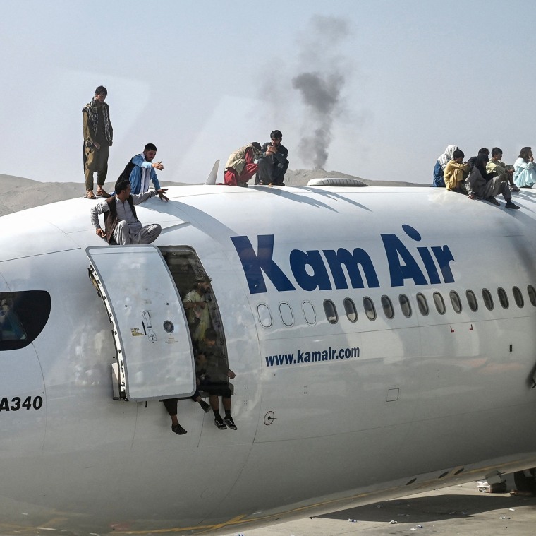 Image: Afghan people climb atop a plane as they wait at the airport in Kabul, Afghanistan.