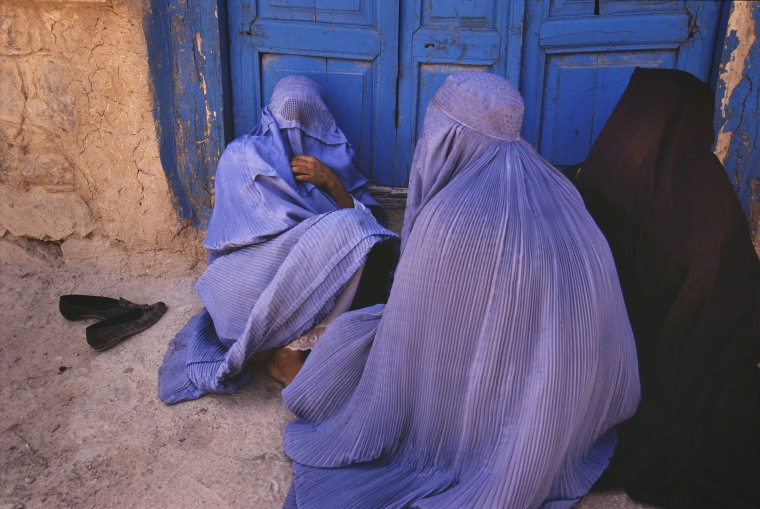 Image: Women dressed in burqas sit outside a door in Herat, Afghanistan, in 1999.