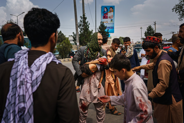 Image: A man carries a bloodied child on the street after Taliban fighters use guns fire, whips, sticks and sharp objects to maintain crowd control over thousands of Afghans who continue to wait outside the Kabul Airport