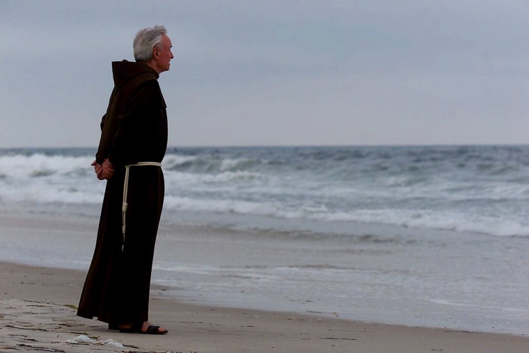 The Rev. Mychal Judge stands at the shore before a service where 230 candles were lit for the victims of TWA Flight 800, at Smith Point Park in Shirley, N.Y., on July 17, 2000.
