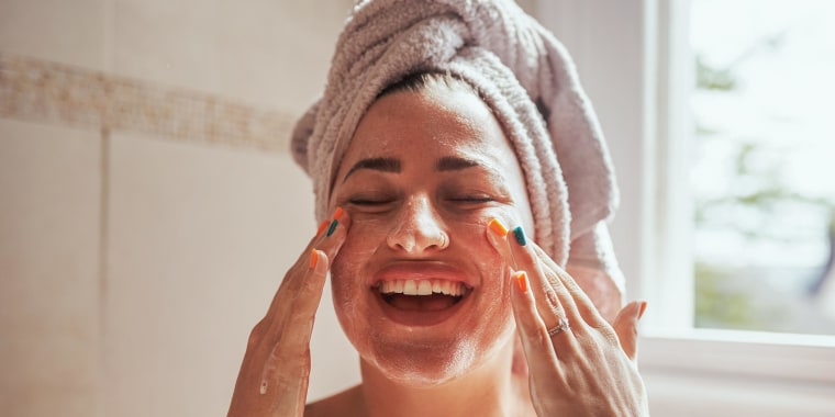 Woman smiling and scrubbing her face in the bathroom