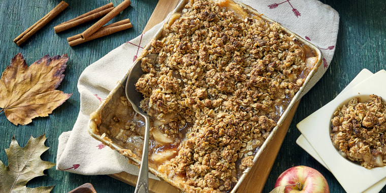Autumn themed overhead view of baked apple crisp with oat crumble topping. With maple leaves & acorns