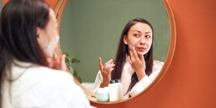 Woman applying moisture cream on her face, while looking in mirror