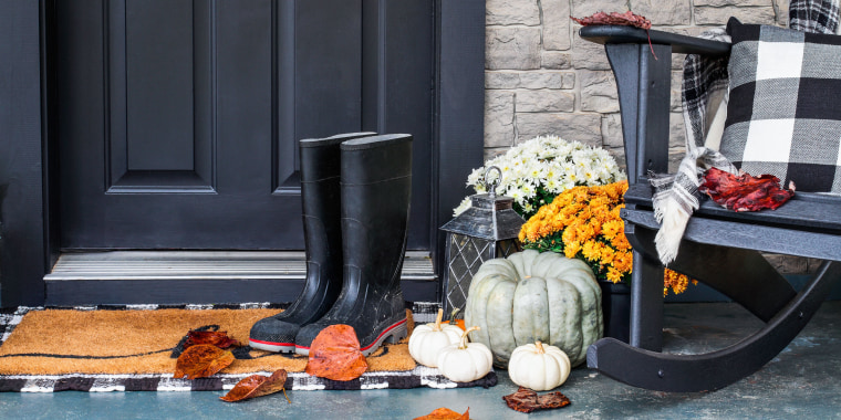 Traditional style front porch decorated for autumn with rain boots, heirloom gourds, white pumpkins, mums and rocking chair with buffalo plaid pillow and throw blanket giving an inviting atmosphere.