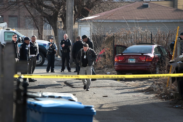 Image: Police look over a bullet-riddled car.