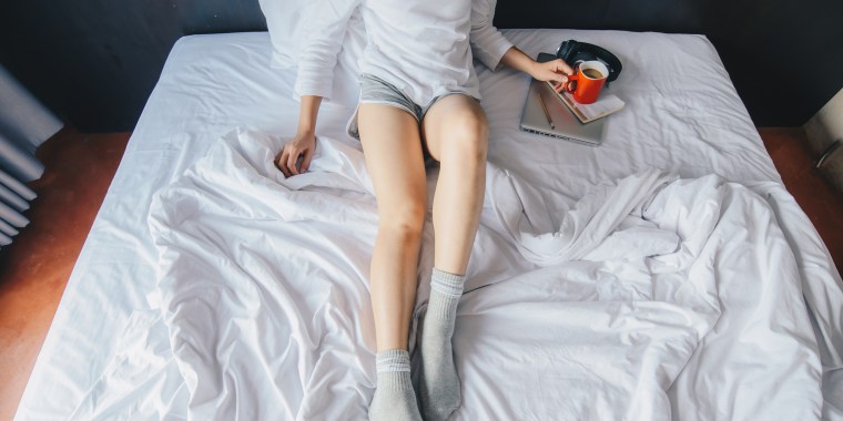 Woman laying in bed with cozy socks and a mug on her laptop