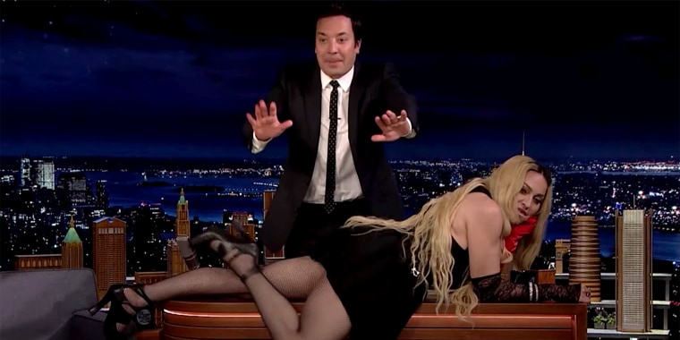 Pop star Madonna drapes herself across TV host Jimmy Fallon's desk in an episode that aired on Oct. 7, 2021.