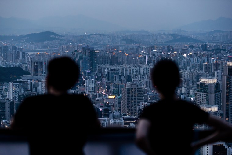 People look at a city skyline from an observation deck of Woomyeon mountain at dusk in Seoul, South Korea, on July 9, 2020.