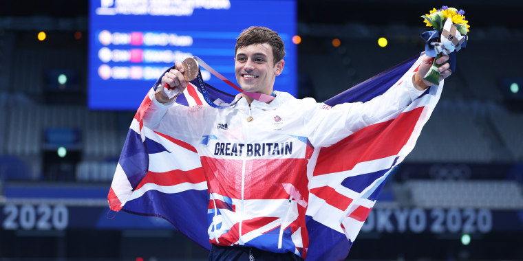 Tom Daley wears the flag of great britain and poses with his medal, smiling