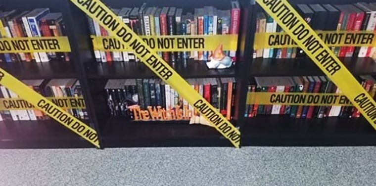 books on a shelf sit behind yellow caution tape