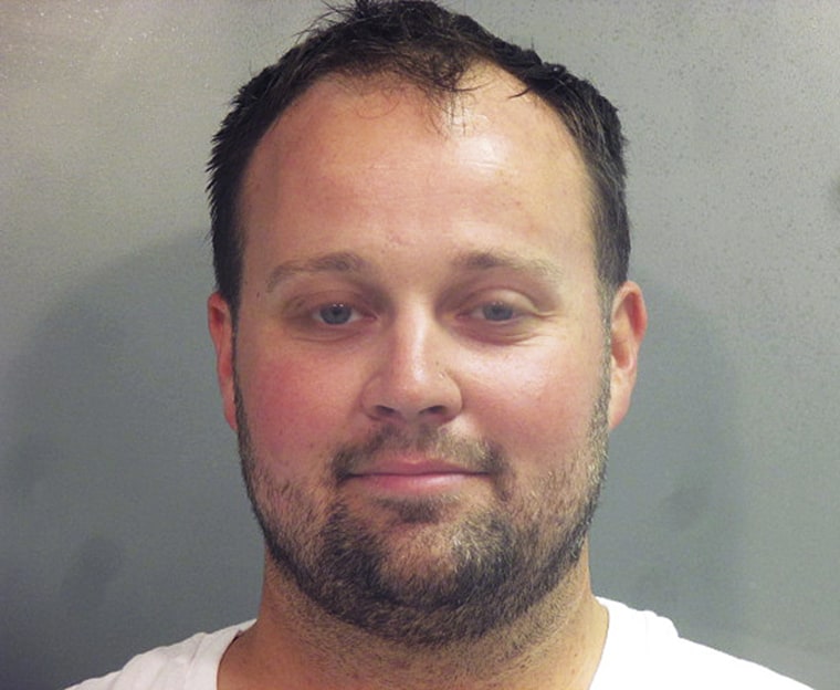 a close up mug shot of josh duggar in a white t-shirt, smiling against a gray background