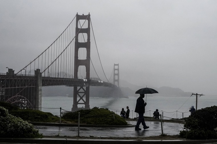 Image: A pedestrian carries an umbrella while walking on a path in front of the Golden Gate Bridge in San Francisco on Oct. 20, 2021.