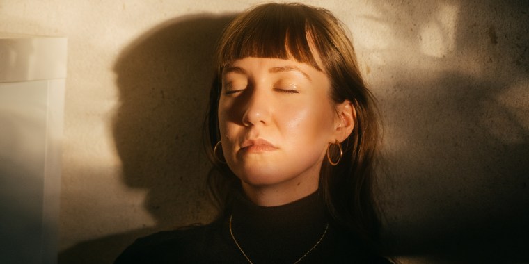 Portrait Of A Young Woman With Her Eyes Closed Sitting Against Wall