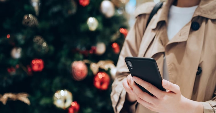 shot of a woman using smartphone in front of a colourful Christmas tree in the festive Christmas season