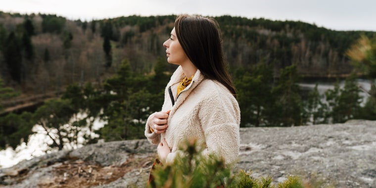 Young woman wearing fleece looking away while standing at mountain during vacation