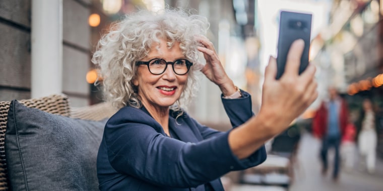 Beautiful senior woman in cafe with curly gray hair taking selfie