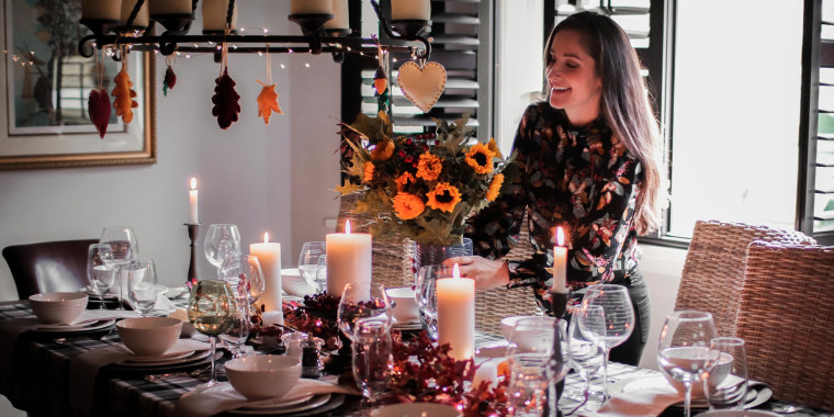 Smiling Mid Adult Woman Holding Arranging Flower Vase On Dinning Table At Home, for Thanksgiving