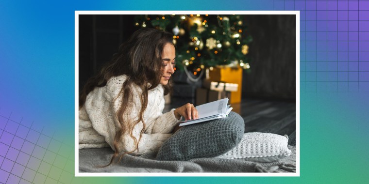 Beautiful woman reading book while relaxing on cushions by Christmas tree at home