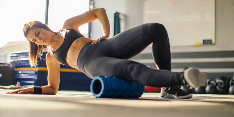Young woman exercising in gym with foam roller