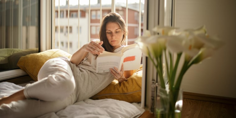 Young woman reading book on bed at home wearing loungewear