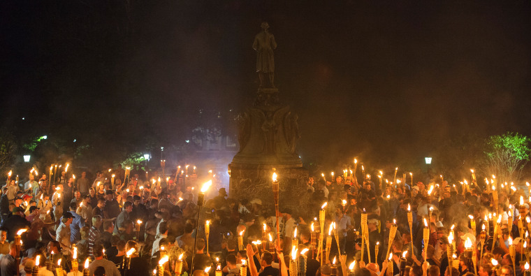 Image: People gather around the base of a statue with torches.
