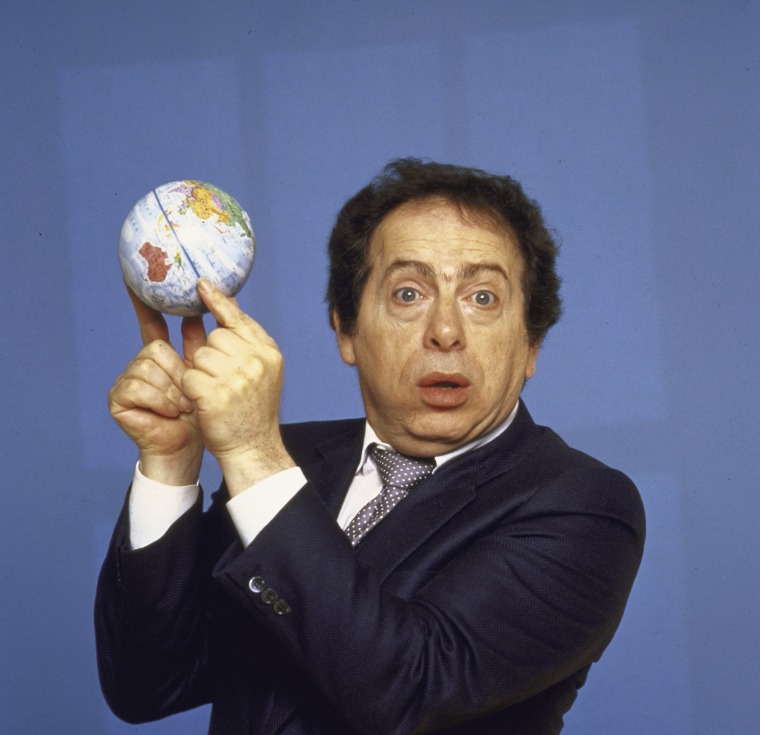 Comedian Jackie Mason holding small globe w tips of his fin