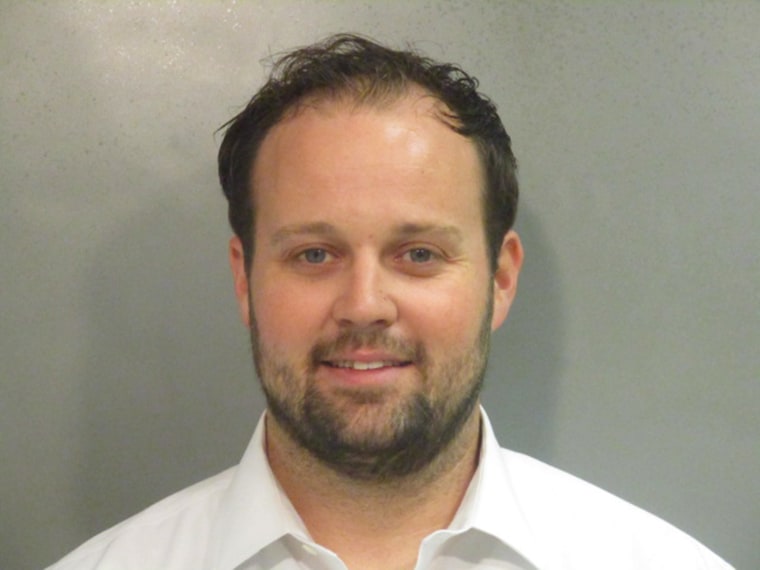 josh duggar in a white button down shirt smiles in a mug shot