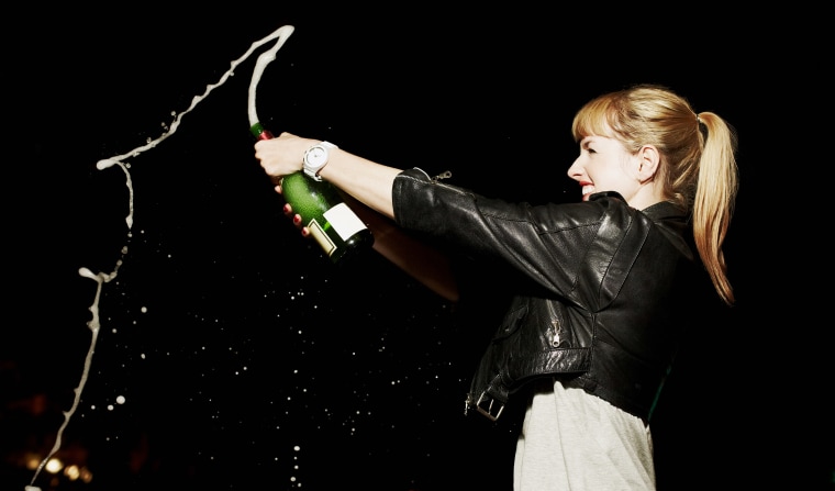 Woman standing alone holding exploding champagne bottle.