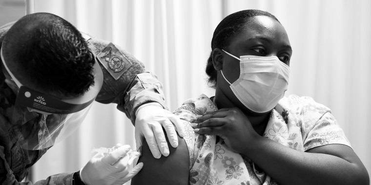 Image: A person wearing scrubs receiving a vaccine.