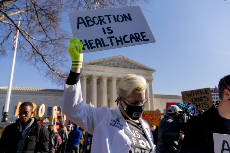 Image: A woman holds a sign that reads \"Abortion is Healthcare\" as abortion rights advocates and anti-abortion protesters demonstrate in front of the Supreme Court on Dec. 1, 2021.