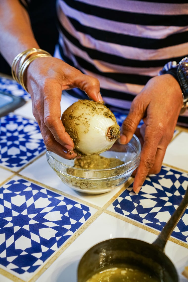 Harris rolls the onion in the butter mixture and then in the spice mixture, then stuffs it into the chicken.