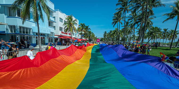 Image: A multi-colored pride flag flies as people participate in the Pride Parade in Miami.