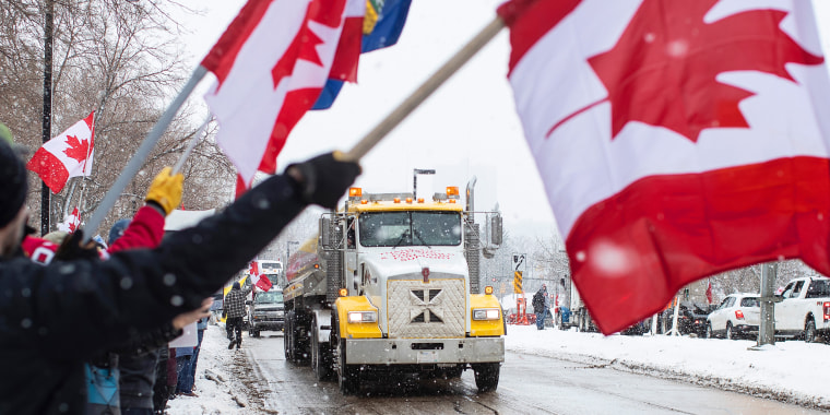 Image: People waving the Canadian flag in protest as a truck passes by.