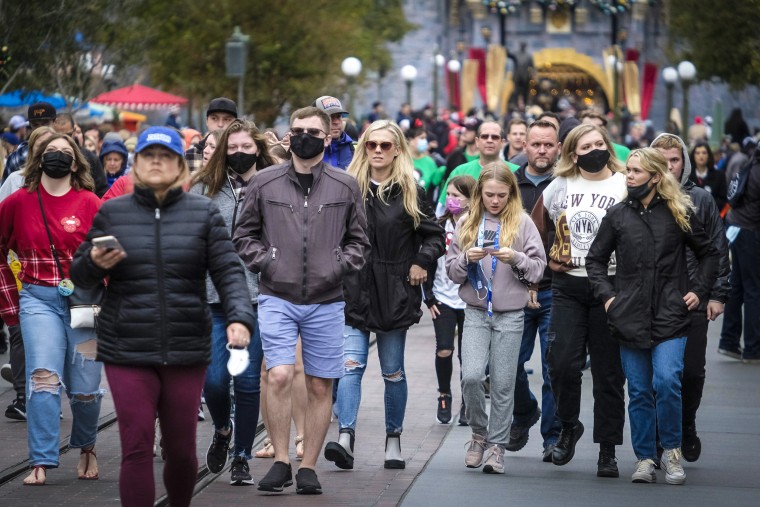 Visitors, some wearing face masks, others not, walk down Main Street USA at Disneyland in Anaheim, Calif., on Dec. 27, 2021.